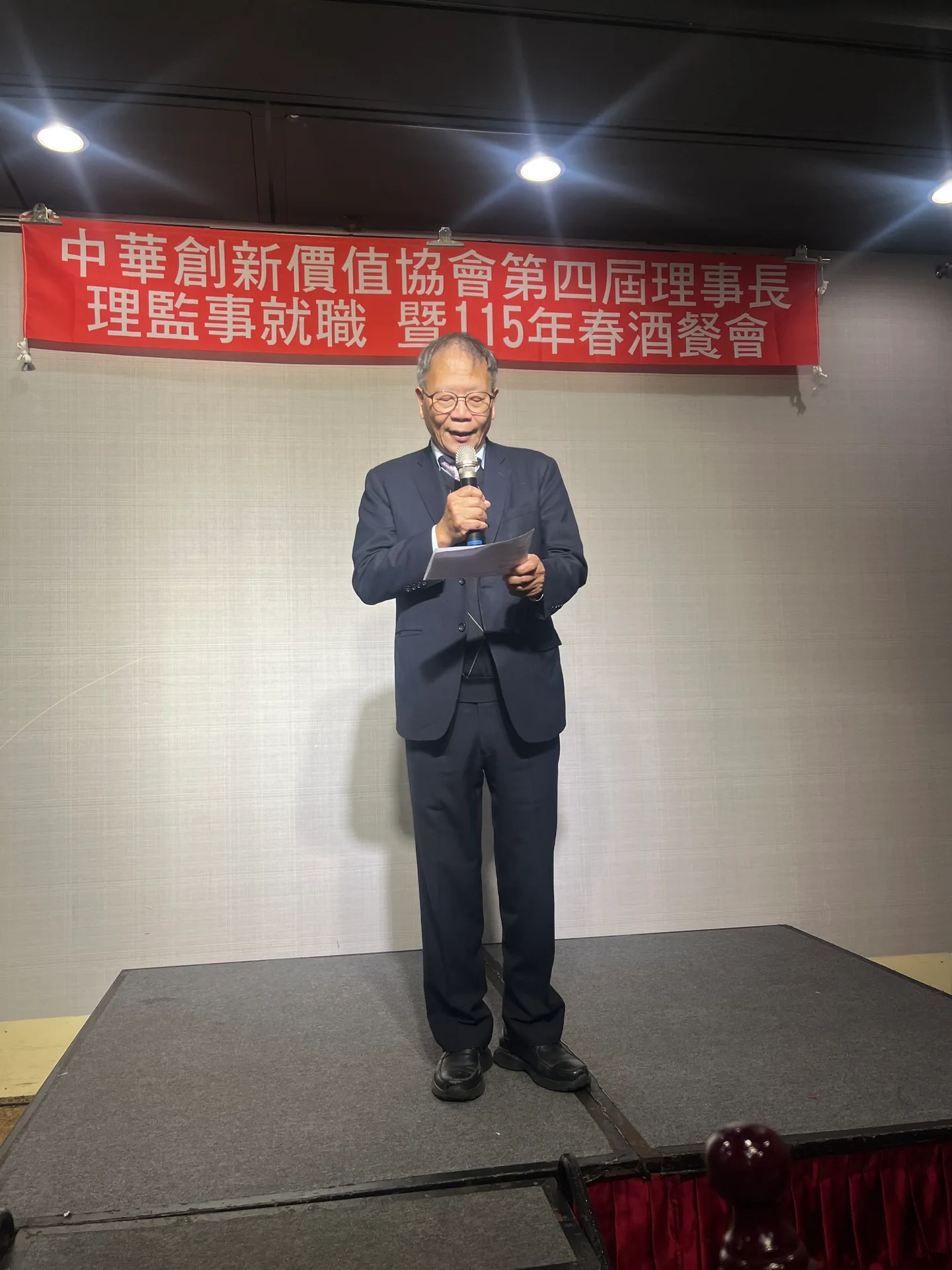 中華創新價值協會第四屆理事長、理監事就職暨115年春酒餐會，講者於舞台手持麥克風致詞